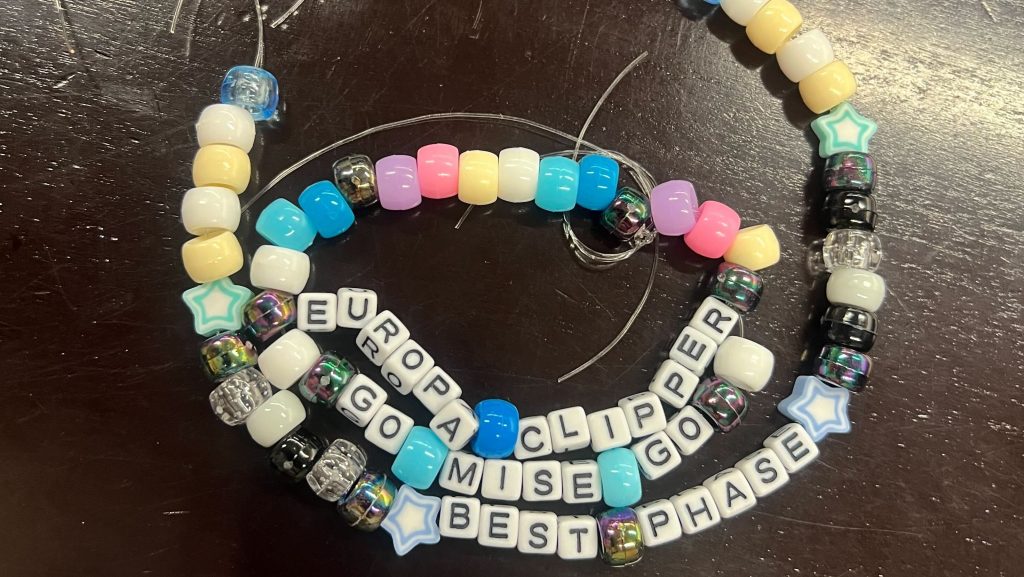 A beaded, multi-colored necklace with the words Europa Clipper Go MISE Go Best Phase on it.