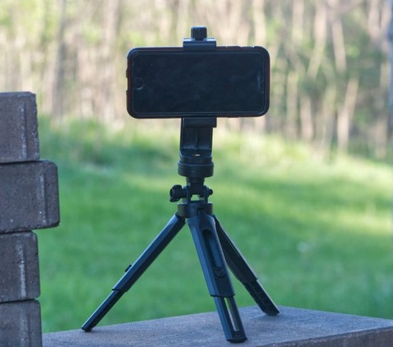 An image of a smartphone on a small tripod, on top of a ledge, facing a grassy field.