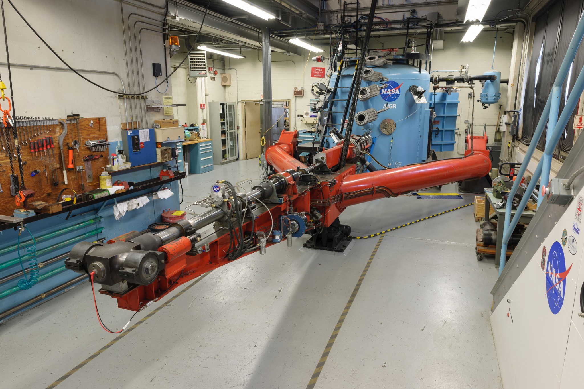 An orange, tuning-fork shaped device facing a blue tank with a NASA logo on its side.