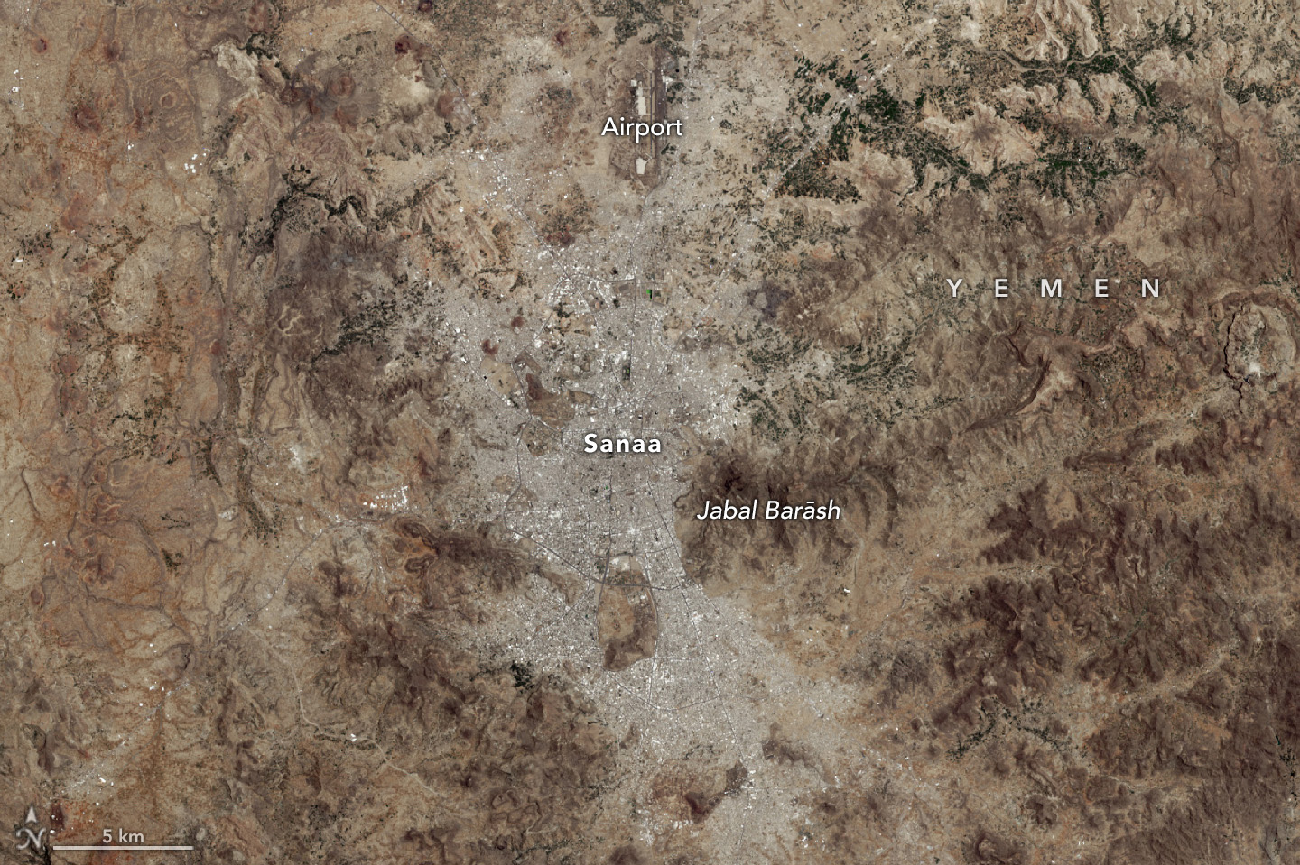 As seen from space: Sanaa, Yemen, and surrounding regions, including an airport to the north and mountains on either side. The image is mostly brown and gray, with very little green space in or around Sanaa.