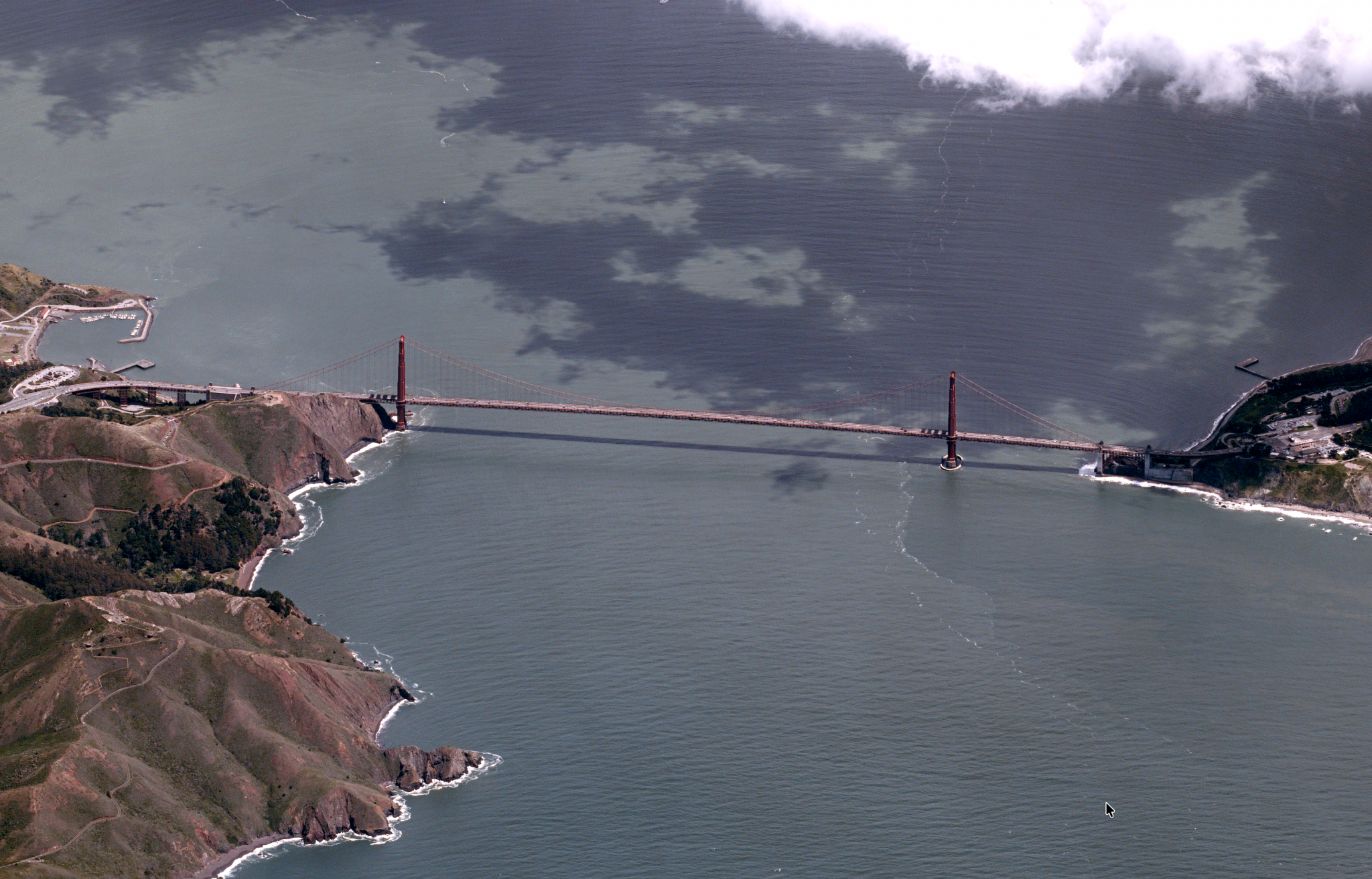 View of the Golden Gate Bridge from above, showing the reddish-brown bridge spanning between two pieces of land, with gray ocean covering most of the scene.