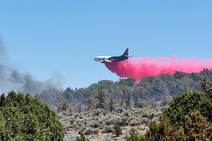 A photograph shows a large air tanker dropping pink flame retardant over brush and short trees in Arizona.