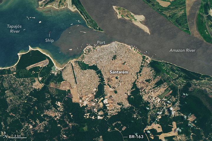 A detailed view shows the city of Santarem and its dense gray-brown urban infrastructure. A port is visible along the city's shore, and several ships appear as small rectangles in the rivers. Green forest around the city is interspersed with roadways.
