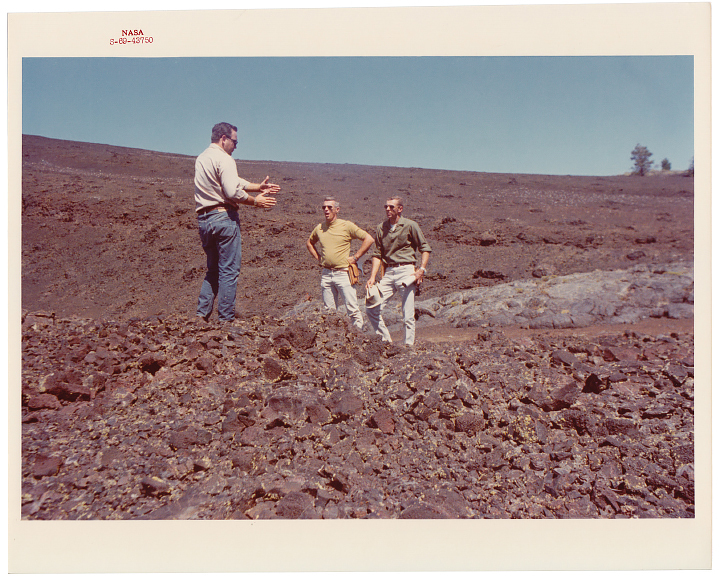 A faded photograph from 1969 shows two plain-clothed Apollo astronauts listening to a geologist while standing on a lava field at Craters of the Moon National Monument.