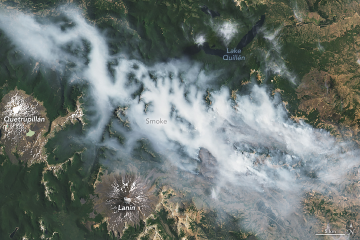 Satellite image of white smoke filling the valleys of a mountainous region of central Argentina. Two snow-capped dormant volcanoes can be seen in the lower part of the image.