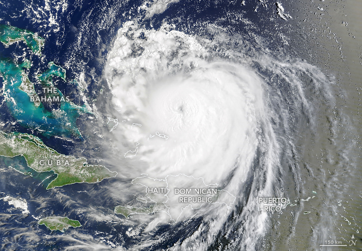A satellite image shows the spiraling clouds of Hurricane Erin over the Atlantic Ocean. Its center, which has a well-defined eye, is located north of Haiti and the Dominican Republic.