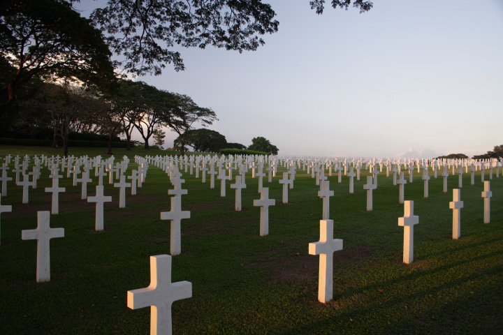 A photograph features several rows of gravestones that look like white crosses on a grassy landscape.