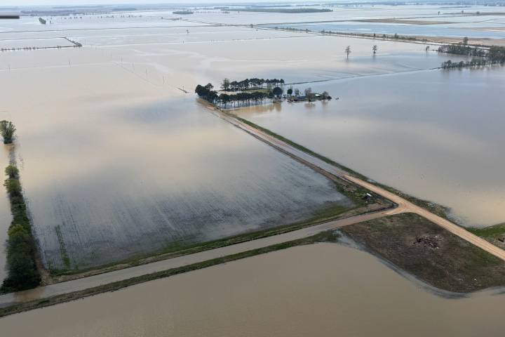 An aerial photograph features several rectangular fields flooded by muddy water. A few roads and trees are also visible.