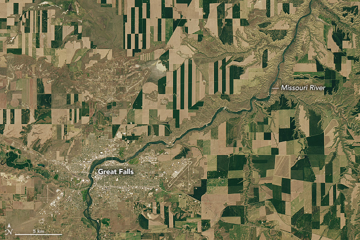 A detailed view of the first image highlights Great Falls and the Missouri River. The urban area toward the bottom-left appears white and gray. Agricultural fields are nestled within the arms of the river and appear in a wide range of shapes, from squares to triangles to rectangles.