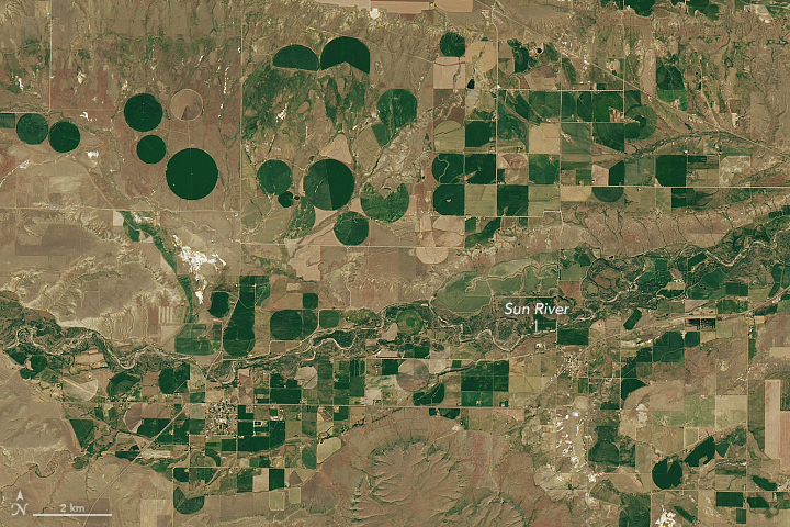 A detailed view of the first image highlights green and brown agricultural fields along the Sun River. This scene displays square fields, as well as numerous circular fields that employ central pivot irrigation.