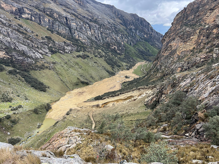 A photo taken from the ground looks down on a river valley with a layer of muddy, rocky material left behind along the banks of the river.