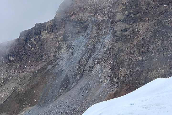 A photo taken from the ground shows a cliff with fresh landslide debris. Gray rocky material is piled up at the lower part of the slope.