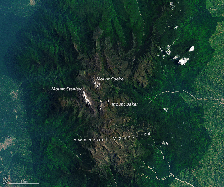 A detailed view of the Rwenzori Mountains, centered in the scene, shows the range's three highest mountains. The peaks are topped with white, much of which is snow.