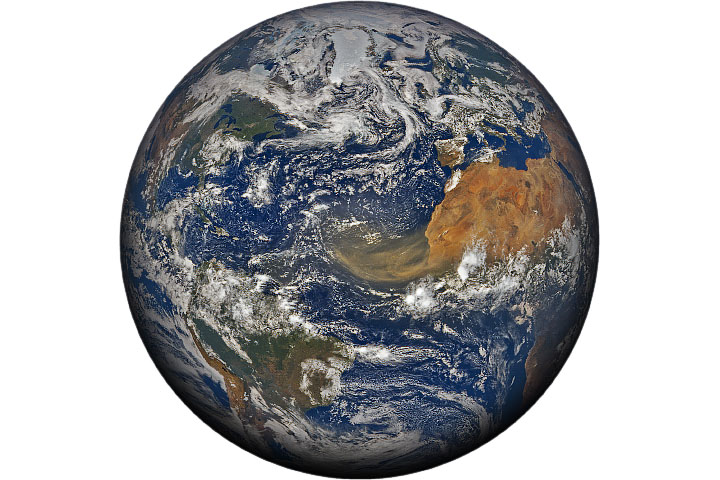 A full-disk satellite image shows a large plume of dust streaming from West Africa over the Atlantic Ocean toward South America. Ice-covered Greenland, scattered clouds over blue oceans, and green landscapes in North America and South America are also visible.