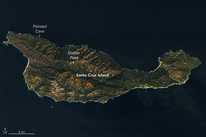 Santa Cruz Island takes up most of the image. The island is mostly green with patches of brown. Diablo Peak lies near the top-left of the island's middle along a distinct ridge. A label indicates the location of a cave along the northwest side of the island's jagged coastline. Dark blue water surrounds the island.