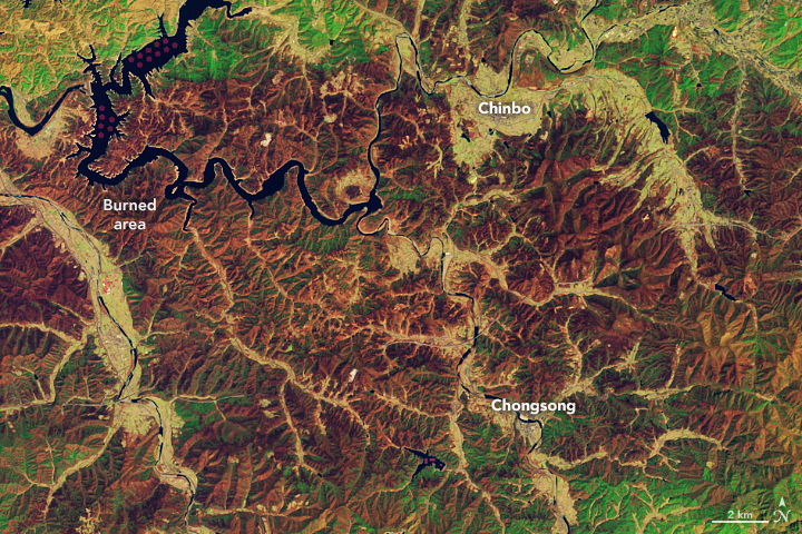 A false-color satellite image shows a detailed view of a middle section of the burned area. Several urban areas lie amid the burned landscape. Dark blue rivers wind through parts of the scene, notably in the top-left corner.