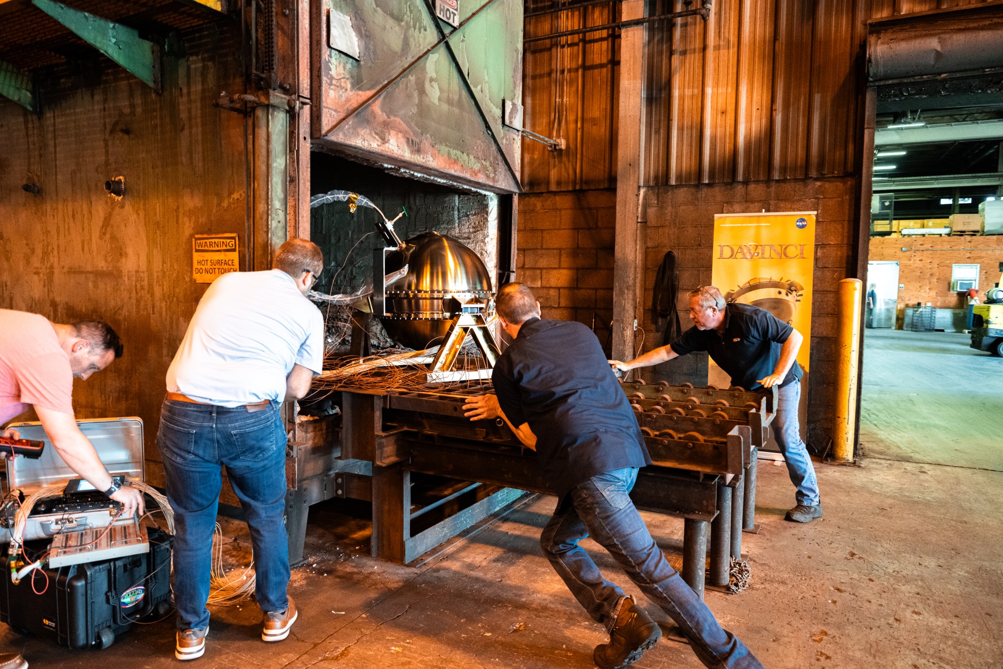 A photo of engineers pushing the DAVINCI descent probe into a furnace