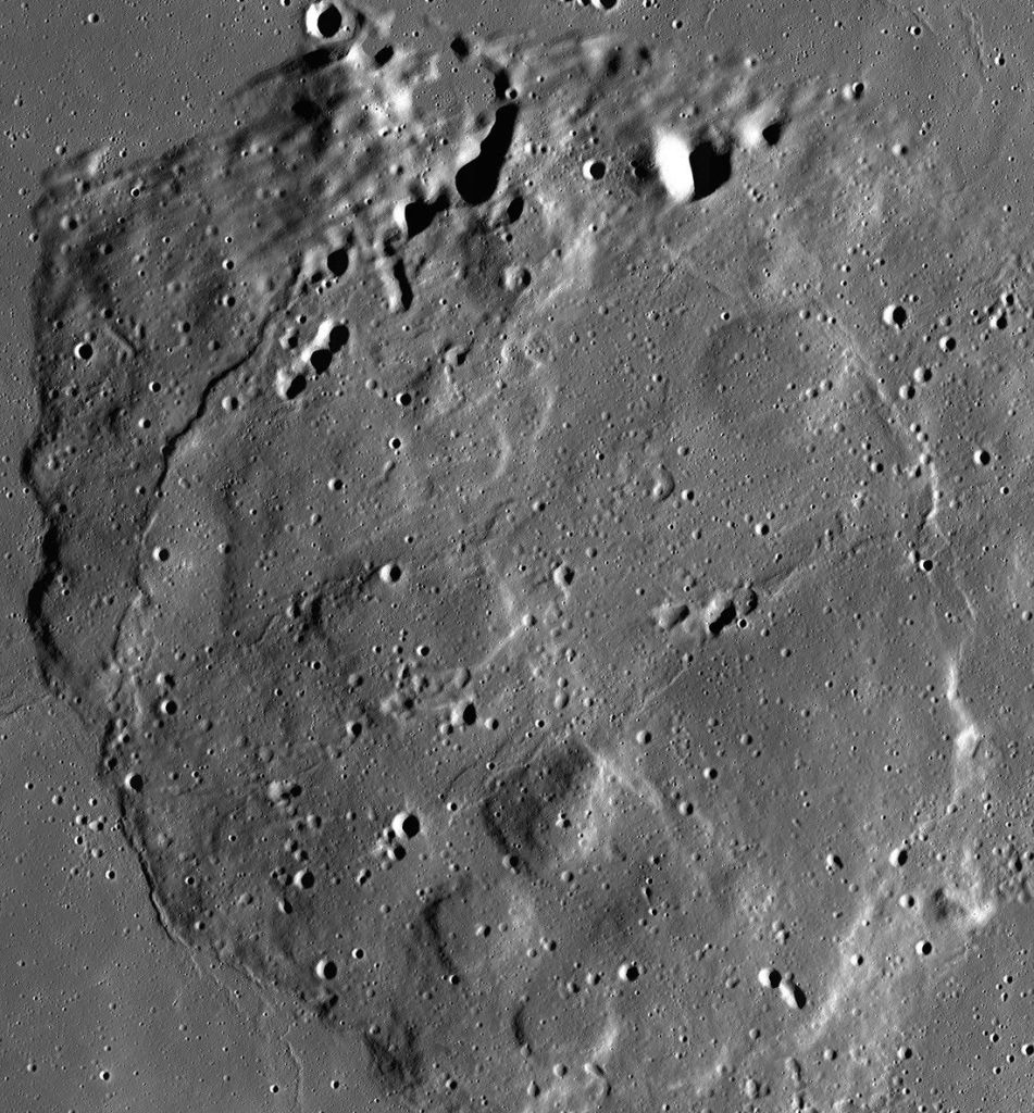 Overhead satellite mosaic showing Mons Rümker, a large, rounded volcanic mound on the Moon's surface surrounded by flat, dark lunar plains. The terrain is marked with impact craters of various sizes, with sharp sunlight casting deep, dark shadows along crater rims and the bumpy, elevated boundaries of the volcanic feature.
